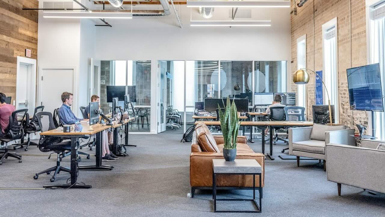 Assess First open plan office with various workers and desks along with a seating area